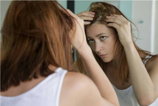 Frau die kritisch ihre Haare im Spiegel betrachtet