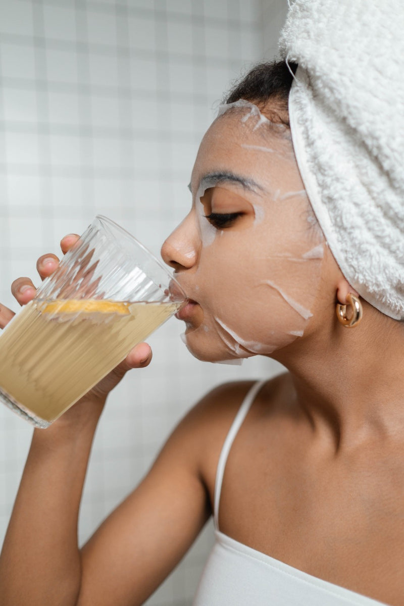 Junge Frau mit Gesichtsmaske genießt ihr NATURTREU Morgenritual Stoffwechsel Getränk.